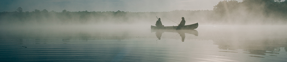 Two fisherman in a canoe on a misty lake at dawn