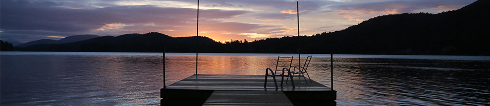 Two chairs sit on a floating dock in a serene lake at sunset